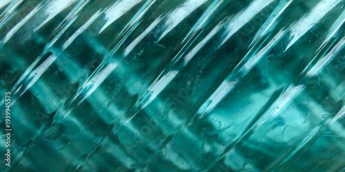 The surface of the bottle or glass container is teal green with an artistic diagonal striped texture and a beautiful light distortion effect.