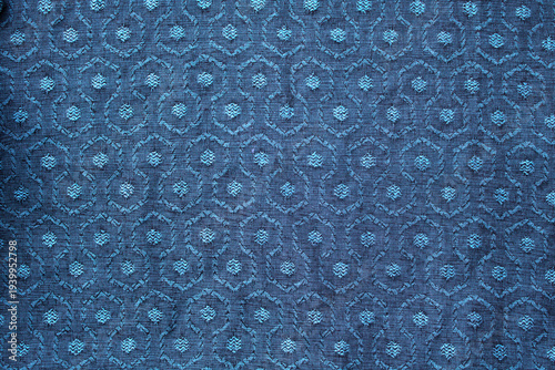 Blue green woven fabric with repeating circular geometric motifs and raised jacquard texture. A seamless textile background .