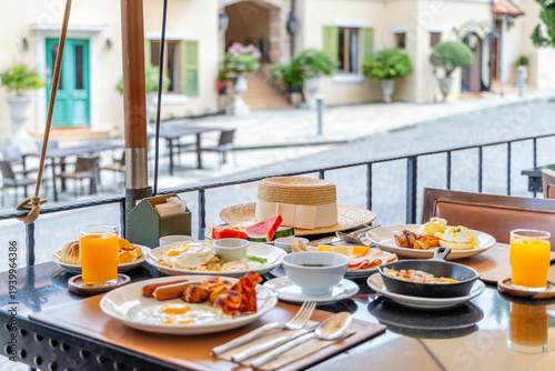 Breakfast table served with eggs, juice and fruit on an outdoor terrace overlooking a cobblestone street. Luxury travel lifestyle and morning dining in a European style village.