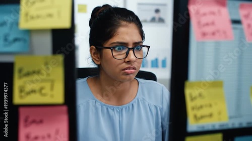 A Young Woman with Glasses Looks Shocked While Working at Her Desk Surrounded by Sticky Notes
