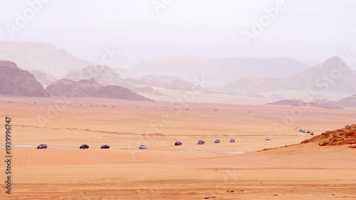 Convoy of off road vehicles crossing Wadi rum desert with dunes mountains remote transport film production logistics concept Jordan