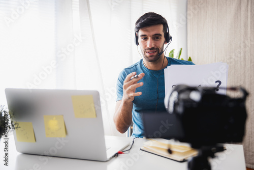 Young man wearing headset talking during online video meeting with laptop and camera