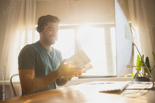Man with headphones holding gift box during online video call at home office