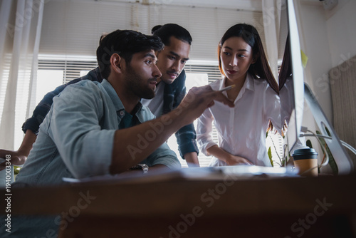 Team of engineers discussing project while pointing at computer screen in modern office