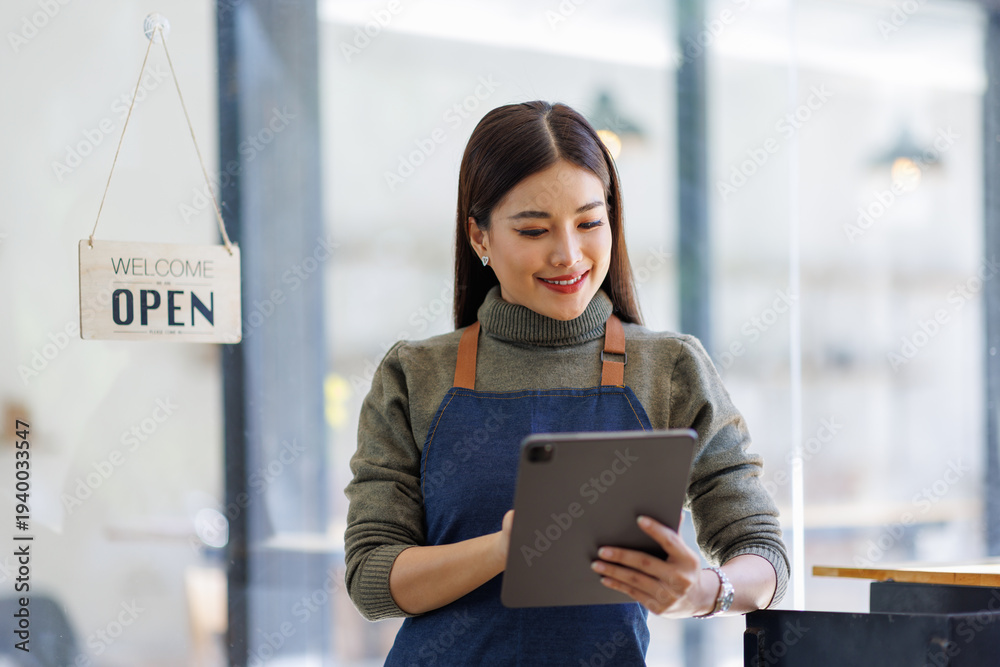 Fototapeta premium This image displays a joyful woman in an apron holding a tablet, exuding warmth and approachability in a retail setting with an open sign prominently displayed.