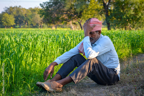 Worried Indian farmer sitting in field holding head in hand due to crop failure or debt