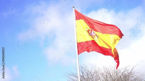 National flag of spain waving proudly in the wind against a beautiful blue sky with soft white clouds, symbolizing spanish pride, patriotism, national identity and european culture