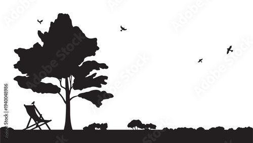 Silhouette of a lone deck chair under a large tree with birds flying in the sky and small bushes on the ground.