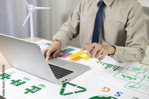 Bilde på lerret Business professionals are analyzing renewable energy charts on their laptops, complete with wind turbine models and green recycling icons, to plan ecological strategies and sustainability data