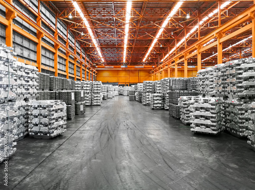 Cuadro en lienzo Interior view of a massive industrial warehouse with organized stacks of aluminum ingots and an orange steel structure