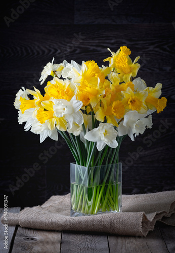 Bright daffodils in a clear vase on a wooden table with dark background in the afternoon light