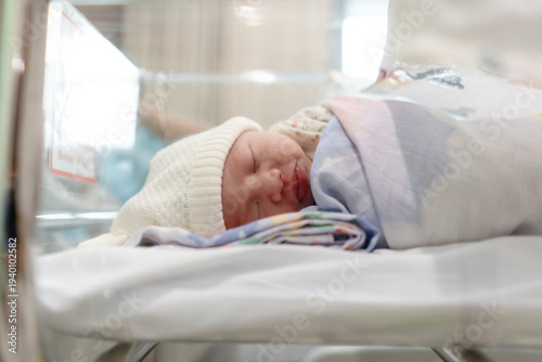 Canvastavla Adorable newborn baby sleeping peacefully in a hospital bassinet, wrapped in a floral swaddle blanket and wearing a white knit hat