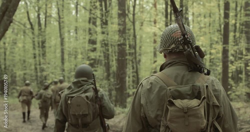 Historical Re-enactment. Re-enactors Dressed As American Soldiers Of USA Infantry Of World War II Marching Walking Along Forest Road In Autumn Day. Group of Soldiers Marching In Forest. Allies Army