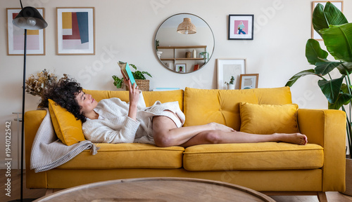 Canvastavla Woman relaxing on yellow sofa reading book