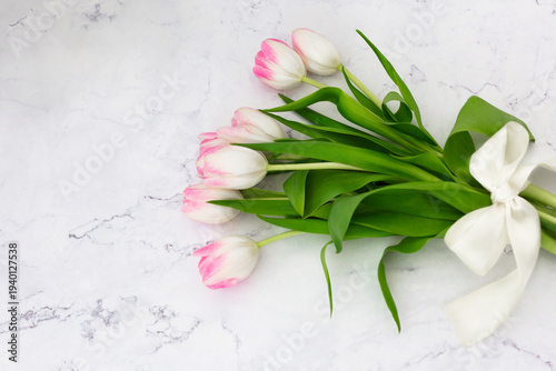 Pink tulips bouquet tied with a white silk ribbon on marble background with copy space.
