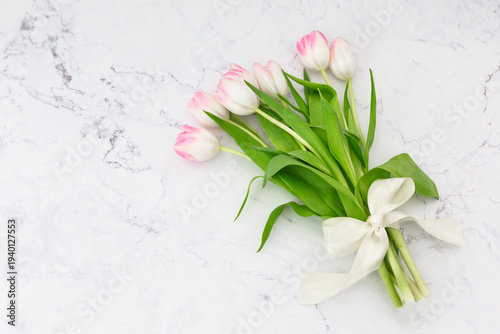 Pink tulips bouquet tied with a white silk ribbon on marble background with copy space.