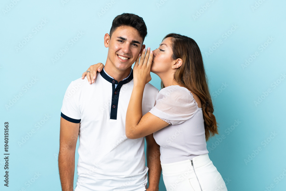 Fototapeta premium Young caucasian couple isolated on blue background whispering something