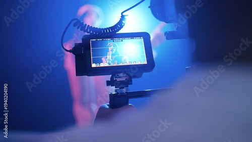 Professional filmmaker operating a camera, shooting a singer performing on a smoky stage with blue and pink lights for a music video production