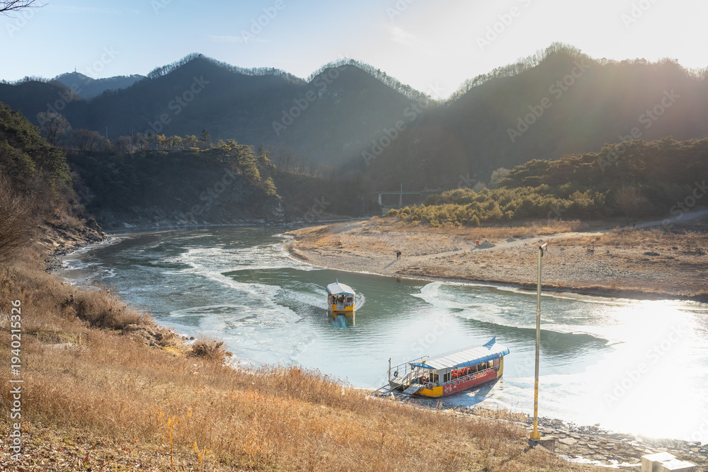 Fototapeta premium Winter Tourism at King Danjong's Exile Site: A Ferry Navigating Icy Waters