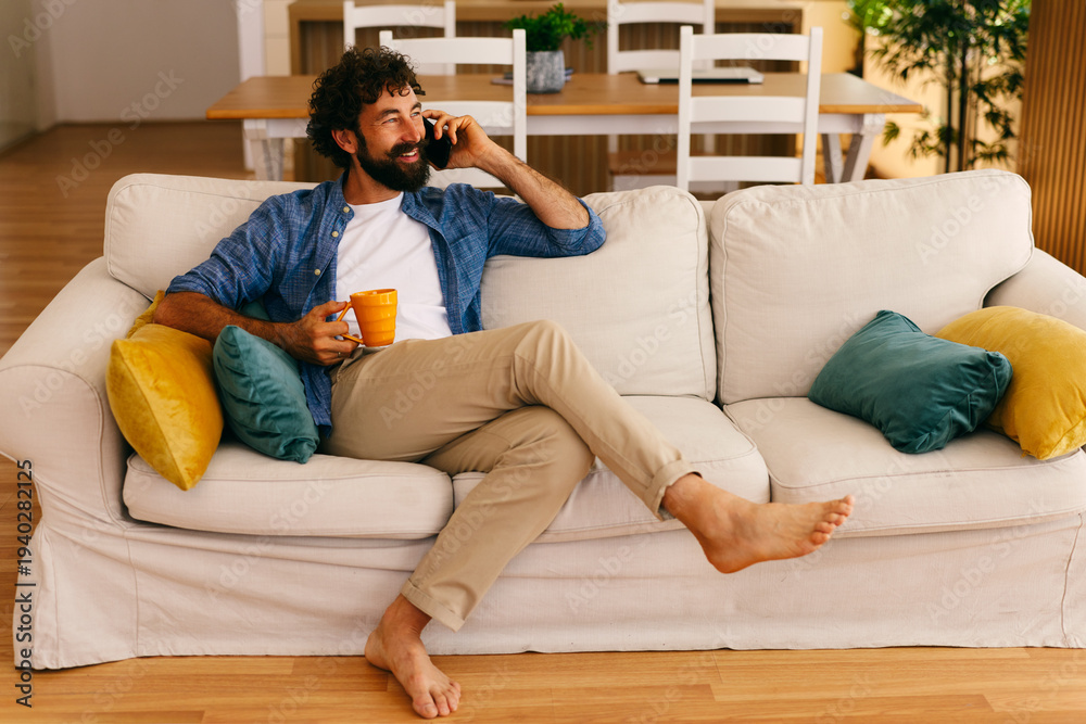 Obraz premium Happy man talking on smartphone while relaxing on sofa