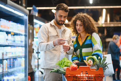 Couple checking shopping list buying groceries in supermarket