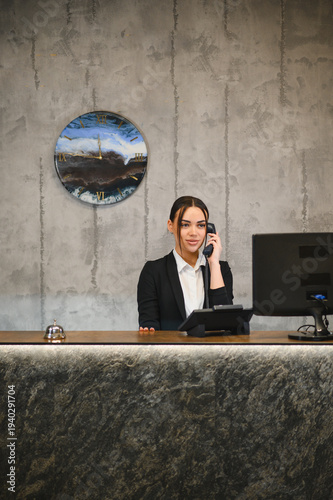 Obraz na plátně Young woman working as hotel receptionist talking on telephone