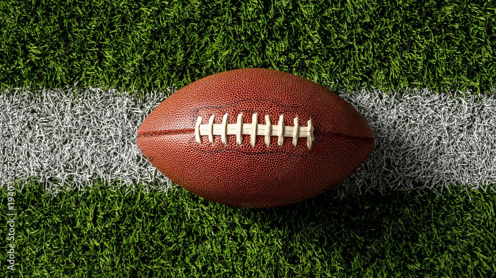 Obraz premium A brown football on green grass with white field markings.