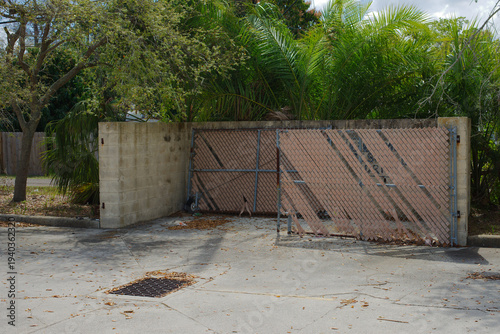 фотографія Worn chain-link gate for dumpster with faded privacy slats leans against a cinde
