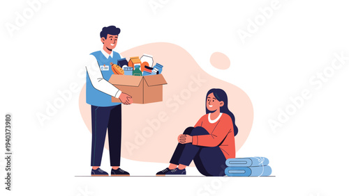 Generous male volunteer in a blue vest giving a cardboard box filled with food supplies to a person sitting on the ground.