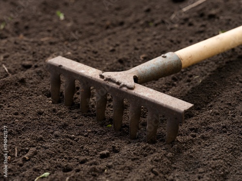 A metal garden rake lying on dark tilled soil.