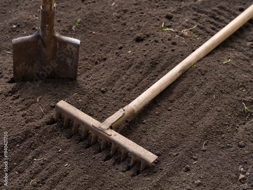A rake and a shovel rest on freshly tilled soil in a garden, prepared for planting.
