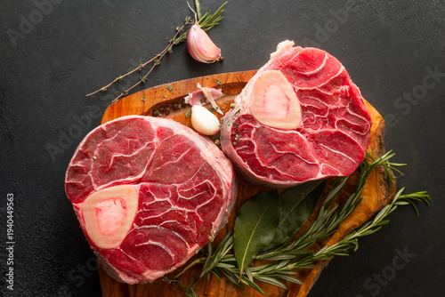 Fotografie Raw osso buco cuts with bone, placed on a rustic wooden cutting board, accompanied by fresh rosemary, thyme, and garlic cloves