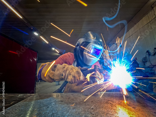 Professional Welder Using MIG-MAG Welding Process with Intense Orange Sparks and Blue Light in Workshop