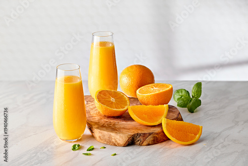 Fresh Orange Juice in Tall Glasses with Mint Leaves and Orange Slices on Wooden Board on Kitchen Counter