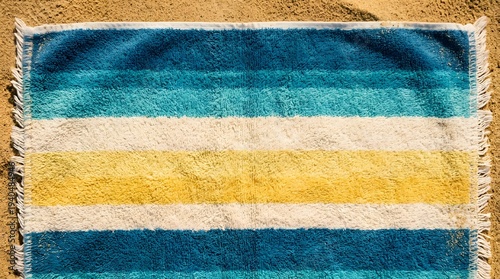 Vibrant striped beach towel on sandy shore with frayed edges