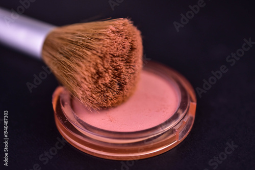 Powder blush (shimmer) and a brush for applying blush on a black background. Close-up.
