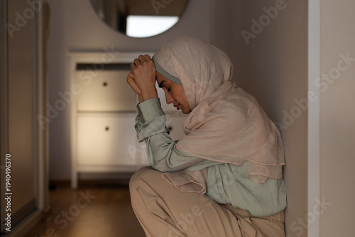 Obraz na płótnie Depressed Muslim woman sitting on floor in hallway with head down, showing signs
