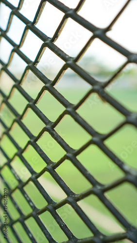 Close up of metal wire fence with blurred green field background