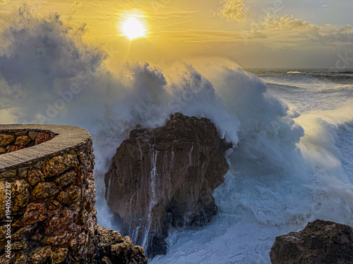 Golden sunset wave crashing into sea stack at Nazare Portugal