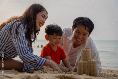 Happy Asian family with a young son enjoying sunset on the beach, playing in the sand and walking together during summer vacation.