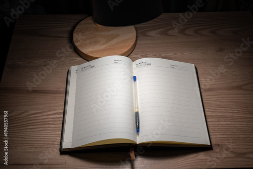 Canvastavla Open blank notebook on wooden desk under warm lamp light.