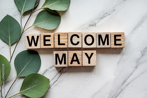 Welcome may text on wooden blocks with eucalyptus leaves, marble background, seasonal greeting, nature concept