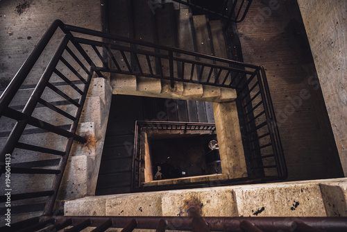 Looking down the center of a twisting stairwell in a parking ramp with trash and dirt