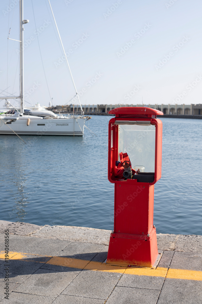 Fototapeta premium Red fire hydrant alongside docked sailboat in acciaroli harbor