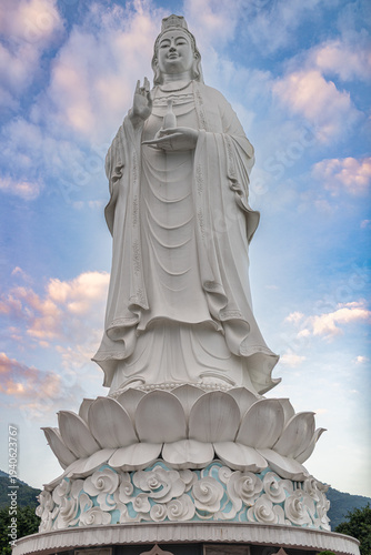 White quan am bodhisattva statue stands on a lotus base against a cloudy sky at linh ung pagoda