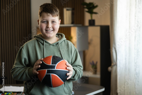 Foto The boy smiles broadly while cradling a basketball in his room , displaying excitement and eagerness to play