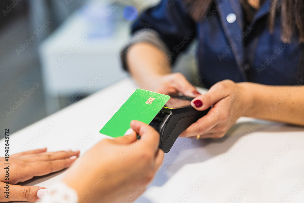 Fototapeta premium Woman holding green credit card tapping pos terminal at beauty salon checkout, contactless payment for service transaction and convenience