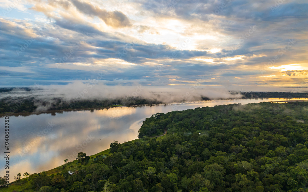 Naklejka premium Panoramic aerial view of the Peruvian Amazon rainforest with dense green canopy stretching to the horizon. Morning mist rises from the tropical jungle as a winding river flows through the vast forest