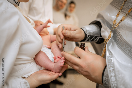 Foto Orthodox priest anointing newborn baby foot with holy oil during baptism ceremon