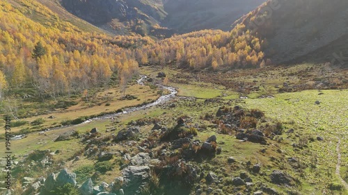 Golden aspens line winding valley stream. Rugged mountains frame sunlit meadows. Rocky outcrops dot the sun-drenched earth. Spectacular autumn light bathes the landscape. Perfect for travel, nature